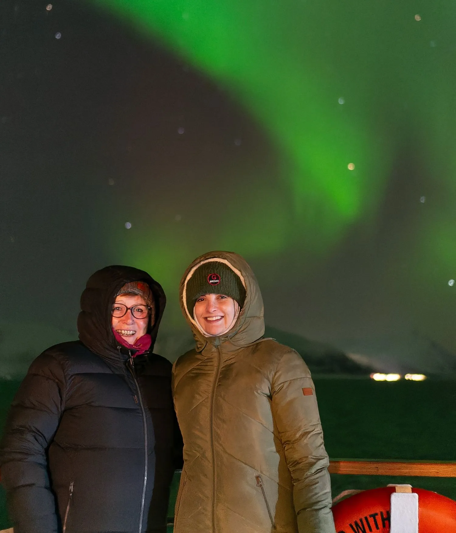 Zwei Frauen in langen Mänteln und lächelnd mit den Nordlichtern im Hintergrund