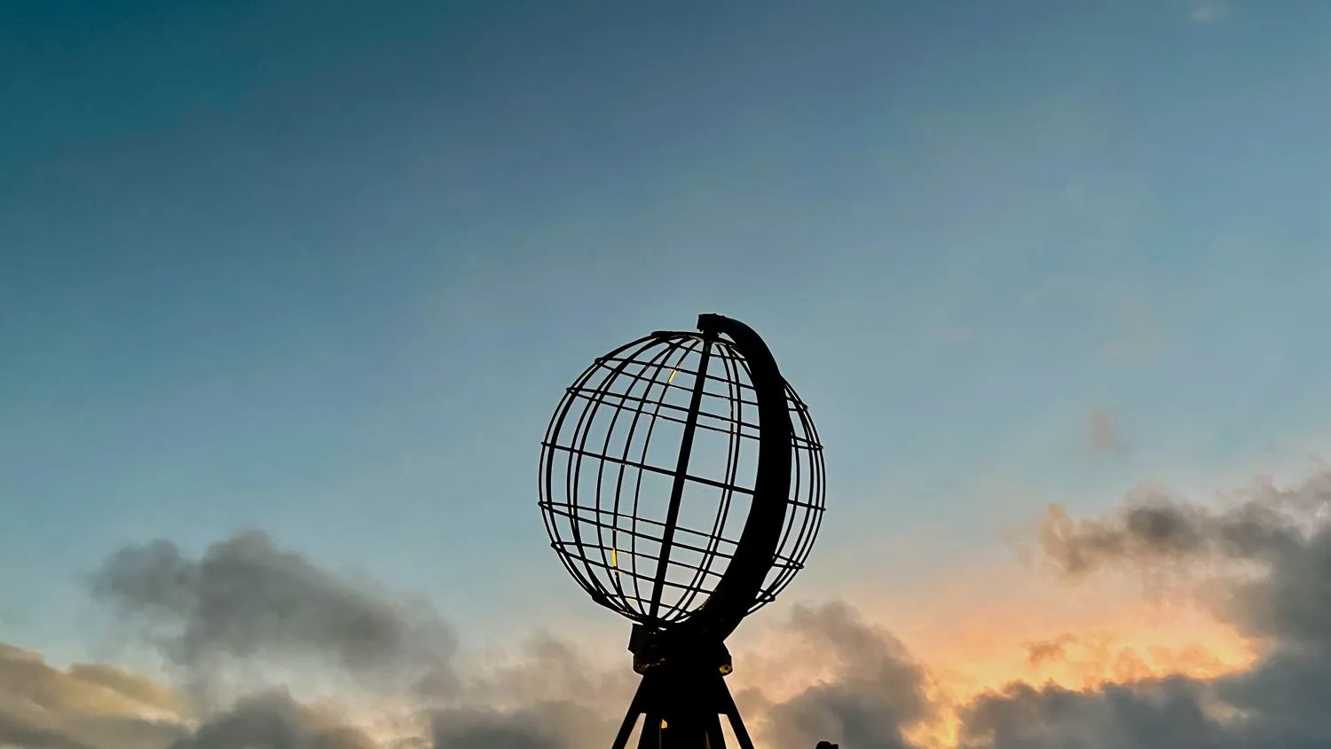 Nordkap-Denkmal mit einer Weltkugel und einem teilweise bewölkten Himmel im Hintergrund