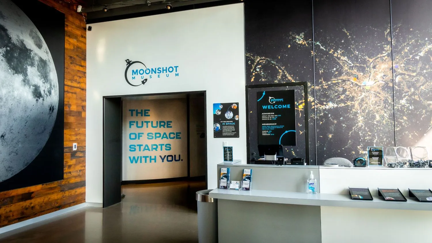 Museumsexponat mit einem großen Foto des Mondes an einer Wand, neben einer Tür, auf der geschrieben steht: Die Zukunft des Weltraums beginnt mit dir.