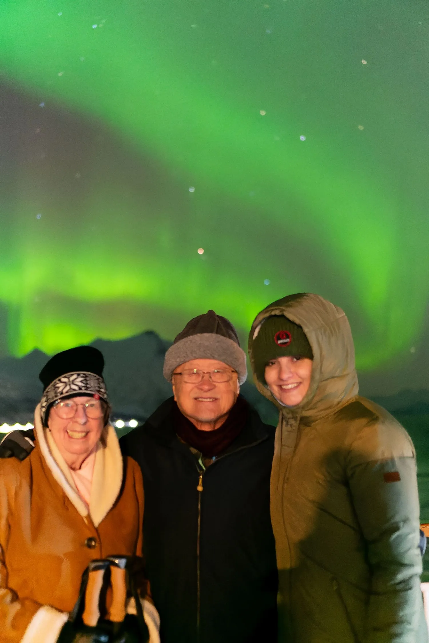 Drei lächelnde Menschen mit dem Nordlicht am Himmel im Hintergrund.
