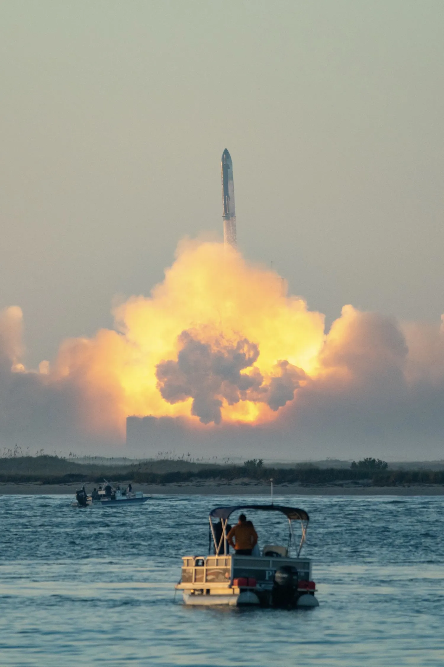 eine riesige rakete erhebt sich aus ihrer rauchfahne in der disatnce. bootsfahrer schauen vom wasser aus zu