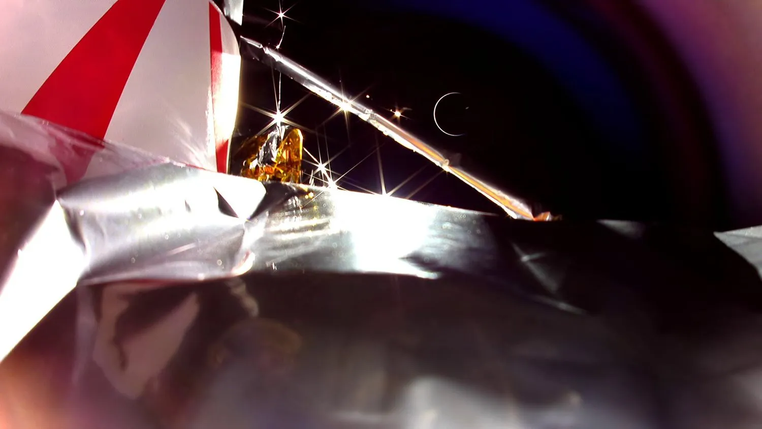 Foto einer Raumsonde, das einen Teil ihrer silbrigen Isolierung mit der Schwärze des Weltraums und der Erdsichel im Hintergrund zeigt