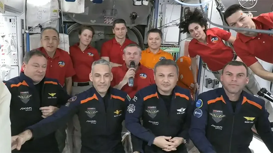 11 Astronauten in blauen und roten Fluganzügen halten eine Willkommenszeremonie auf der internationalen Raumstation ab