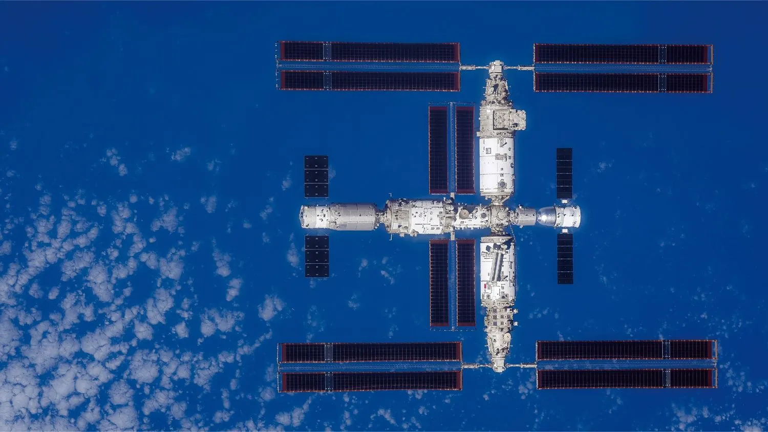 eine große T-förmige Raumstation von oben gesehen mit der Erde darunter