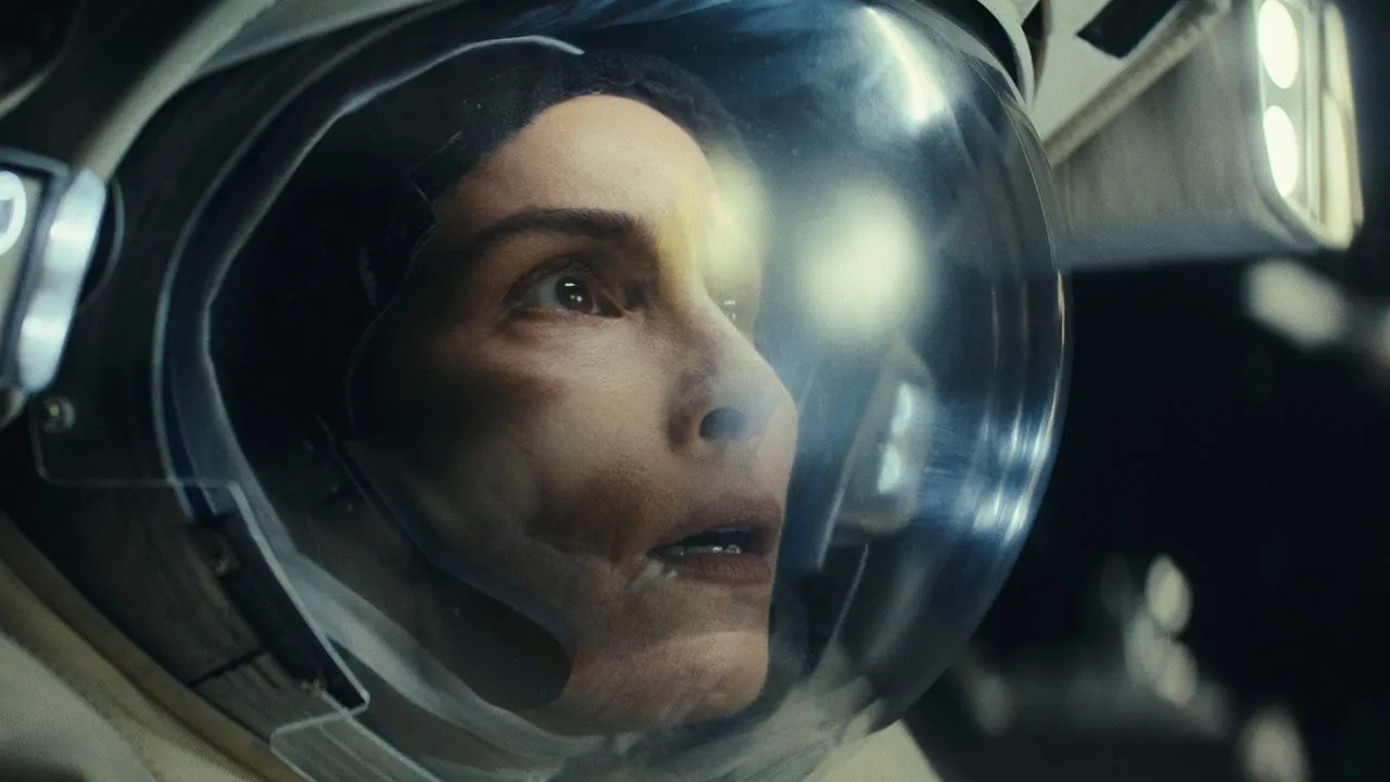 Nahaufnahme des Gesichts einer Frau, die einen Astronautenanzug und einen Helm trägt. Sie ist schockiert, hat große Augen und einen offenen Mund.