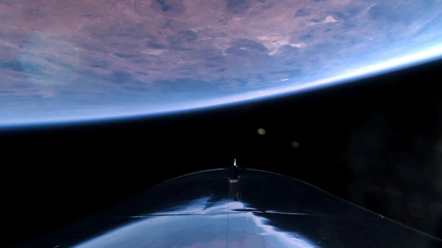 die Kurve der Erde vor der Schwärze des Weltraums, mit einem Teil eines silbernen Raumschiffs im Vordergrund