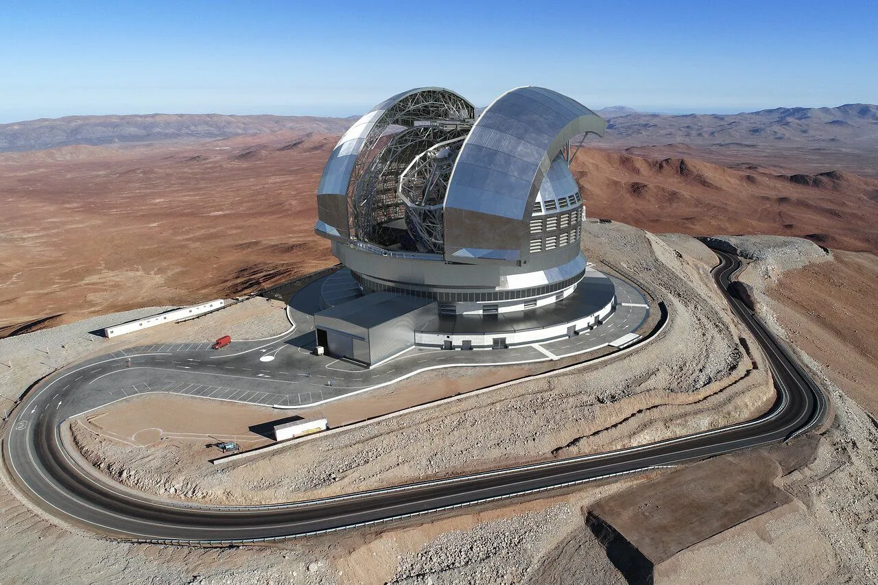 Eine Darstellung, wie der ELT aussehen wird. Es scheint ein metallfarbenes, riesiges Observatorium in einer wüstenähnlichen Region zu sein.