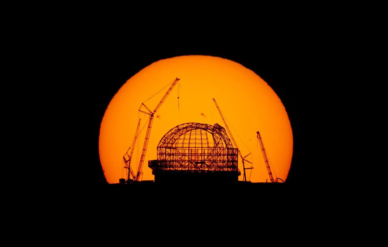 Ein gigantischer Blick auf die Sonne bei Sonnenaufgang hinter einem silhouettierten ELT im Bau.