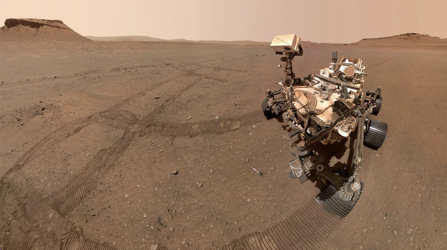 ein großer Marsrover sitzt in einem sandigen Fleck auf dem Roten Planeten, mit einigen seiner Reifenspuren in der Nähe.