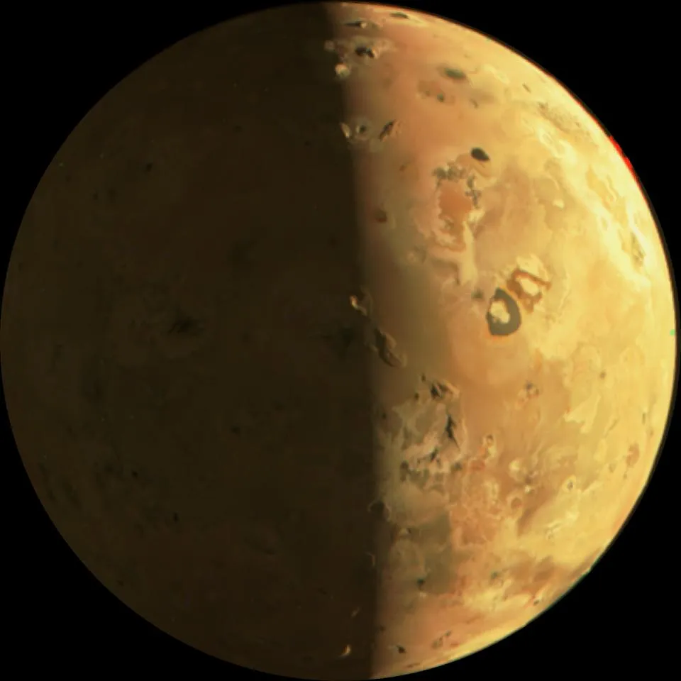 Eine Ansicht von Io. Die rechte Seite ist beleuchtet und die linke ist schattig. Der Mond scheint gelblich zu sein und wirbelförmige Muster zu haben.