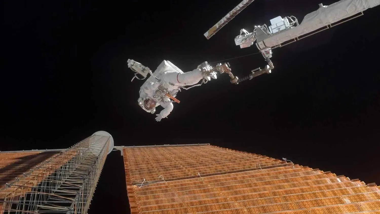 ein Astronaut auf einem Roboterarm neben einem Solarpanel im Weltraum