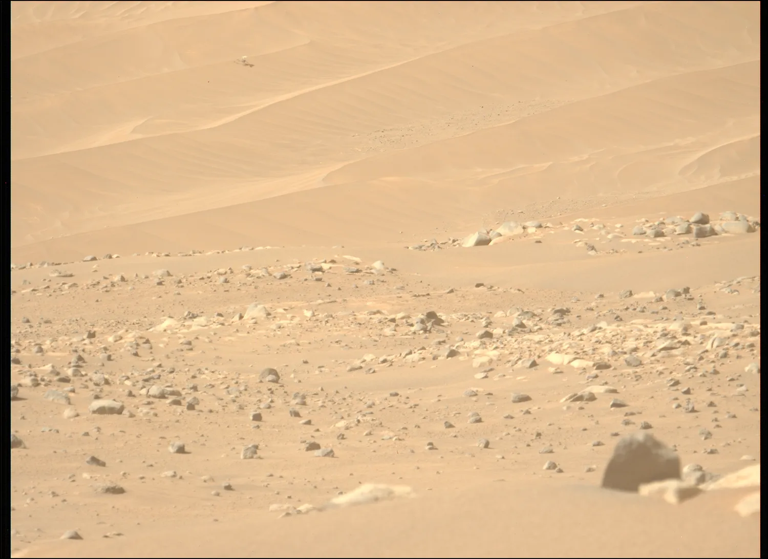 ein kleiner Hubschrauber steht regungslos auf einer Sanddüne in der Ferne, während rote Erde und Felsen die Szene ausfüllen