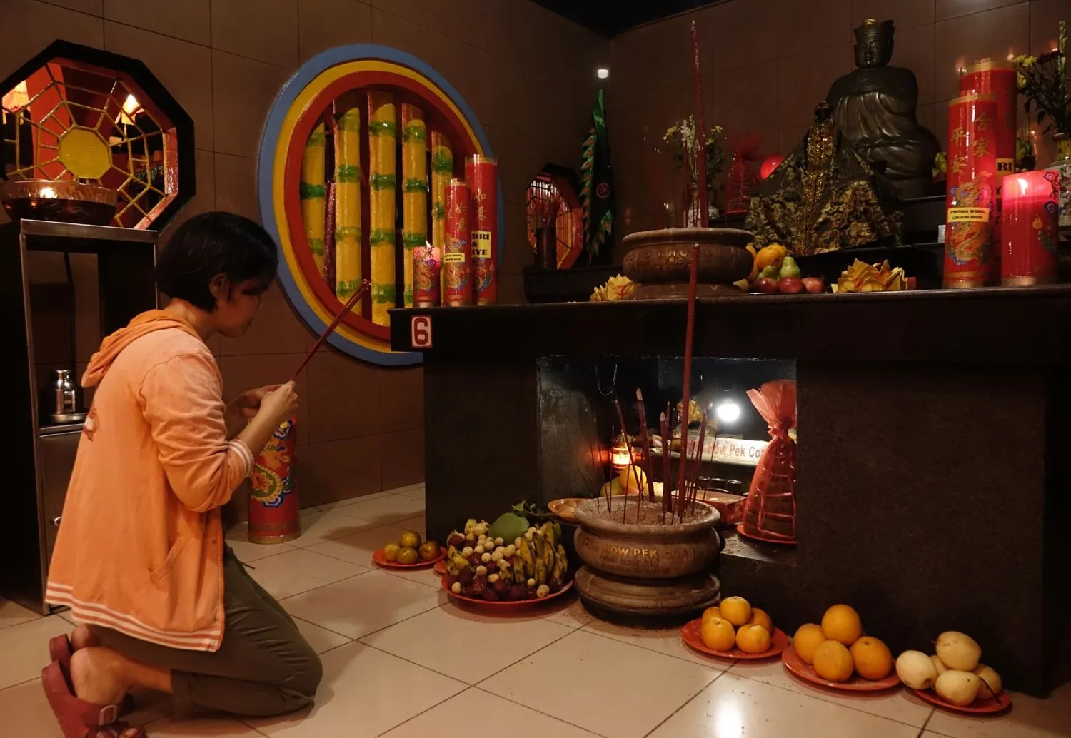eine Frau kniet vor einem mit Früchten und roten Kerzen bedeckten Altar