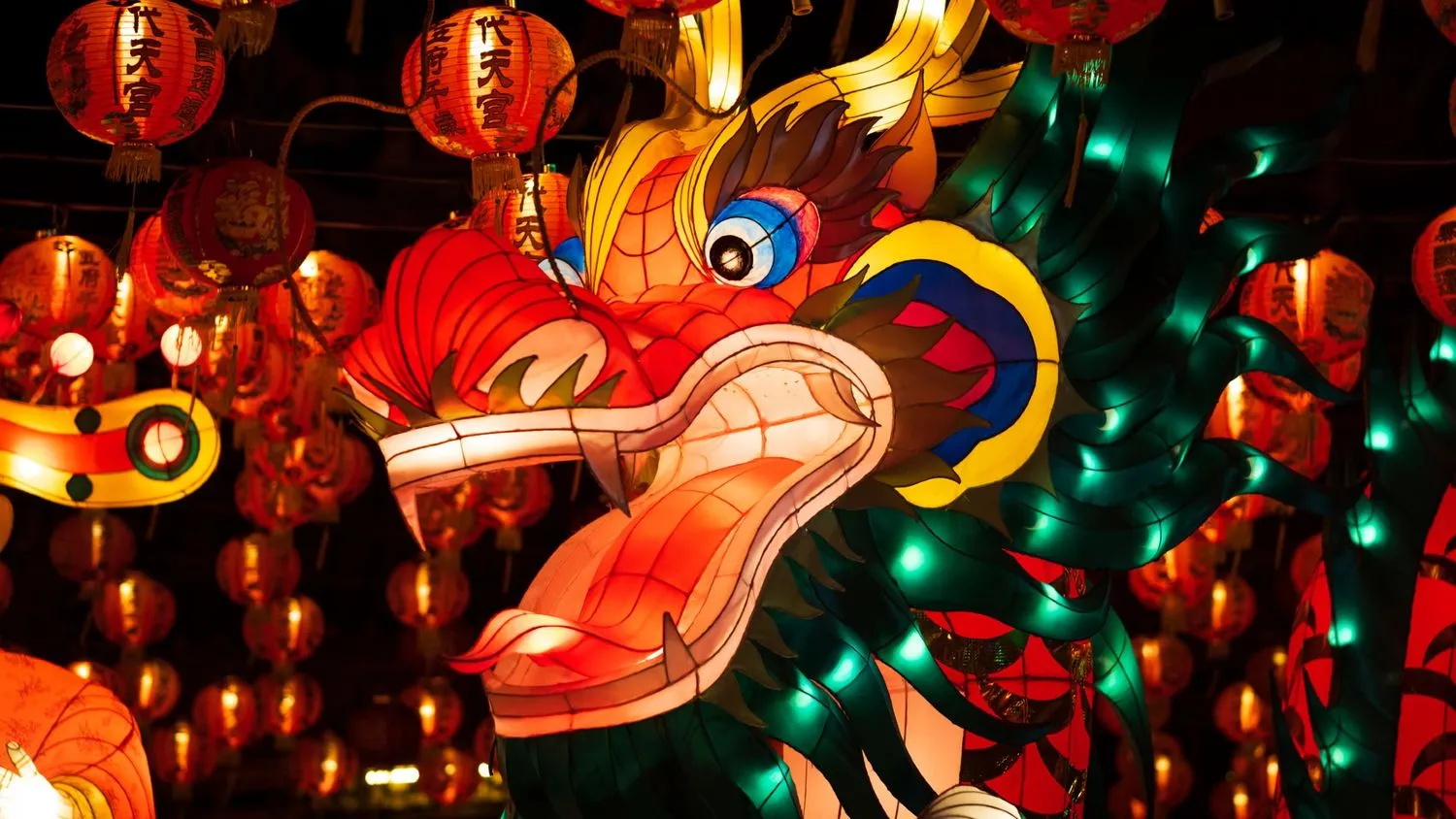 eine leuchtend bunte, drachenförmige Laterne, die nachts beleuchtet wird, umgeben von roten, kugelförmigen Laternen mit chinesischen Schriftzeichen