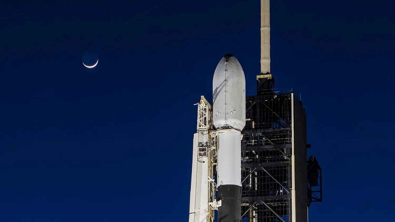 Eine weiß-schwarze Rakete auf der Startrampe mit der Mondsichel am Nachthimmel