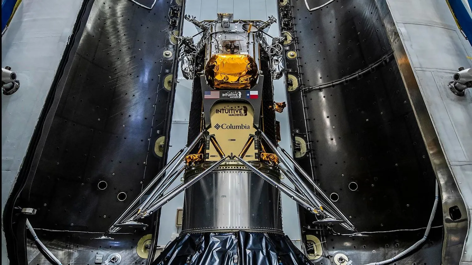 ein zylindrisches Raumfahrzeug mit vier dreieckigen Beinen ist von zwei muschelartigen Hälften einer Raketennutzlastverkleidung in einem Hangar umgeben