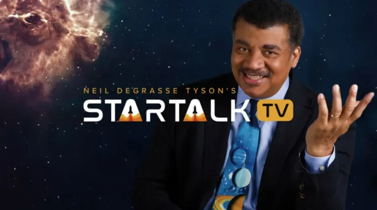 ein Mann im Anzug, der lächelt und eine Krawatte trägt, auf der eine Karte des Sonnensystems abgebildet ist