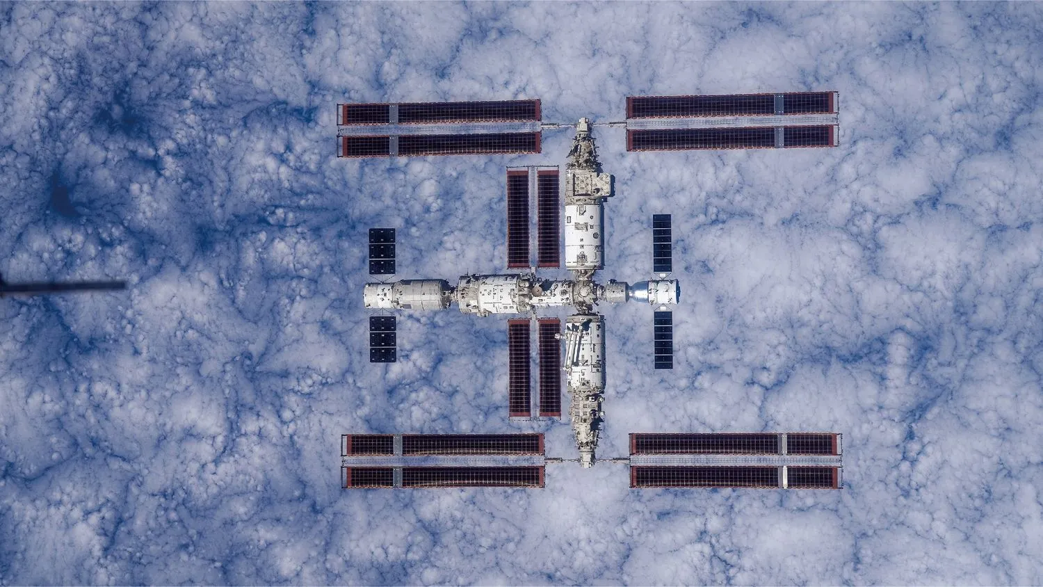 eine große T-förmige Raumstation von oben gesehen mit der Erde unter ihr