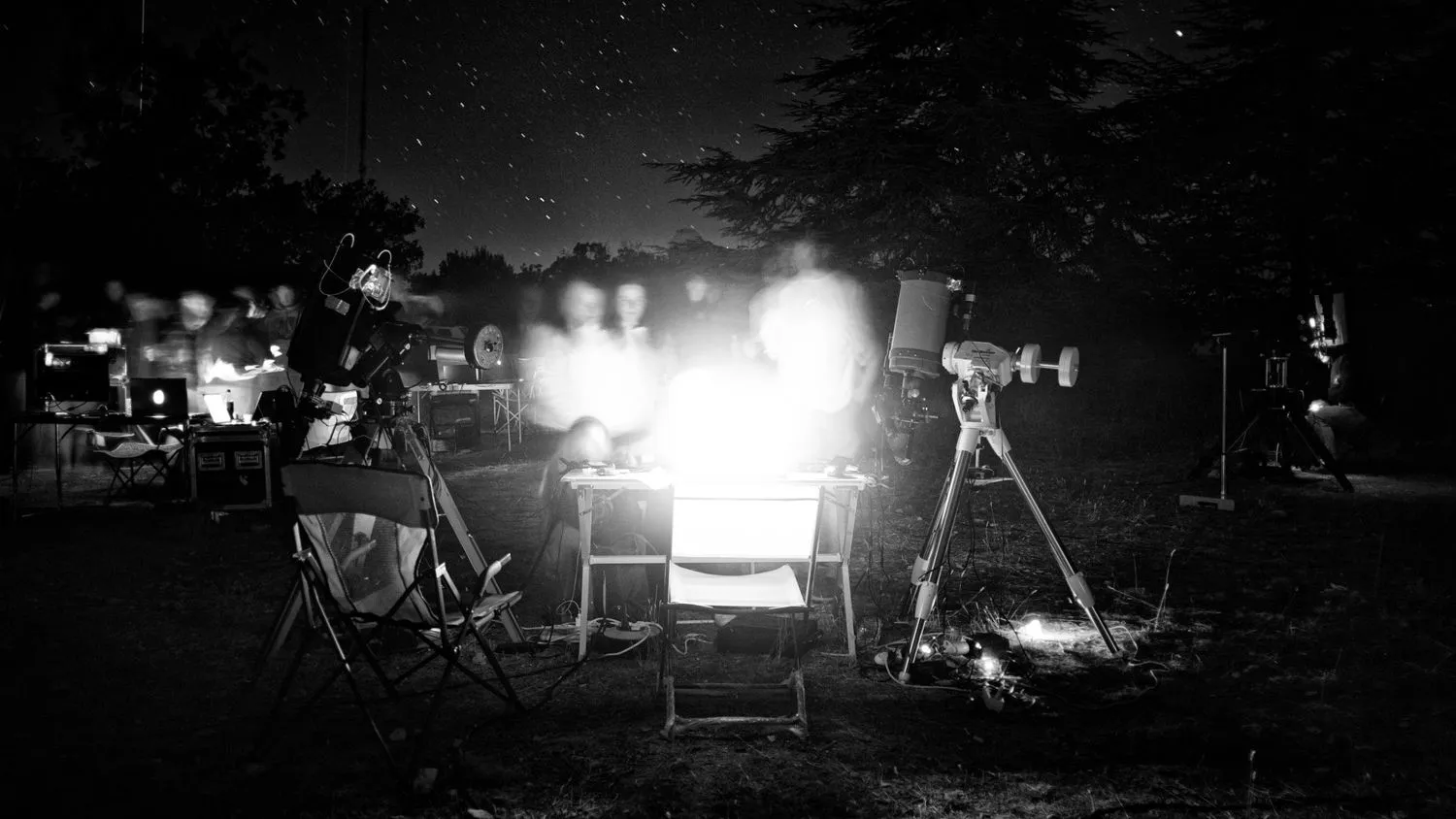 ein Schwarz-Weiß-Foto einer Gruppe von Menschen, die sich um ein Teleskop drängen
