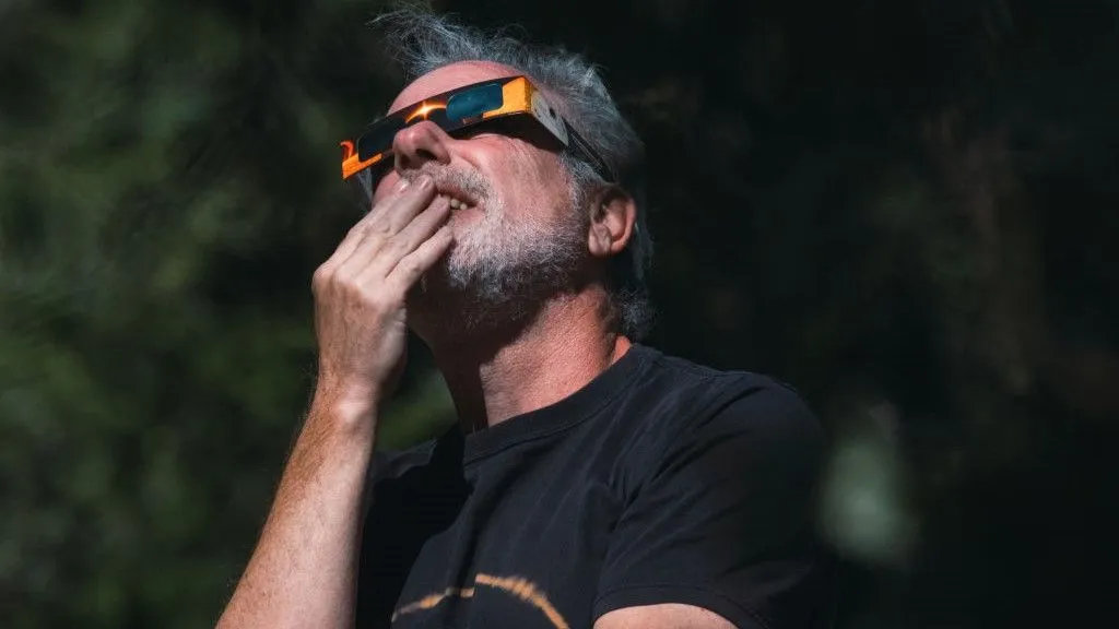 Ein Mann mit einer Sonnenfinsternisbrille blickt in den Himmel und hält sich die Brille an den Mund.