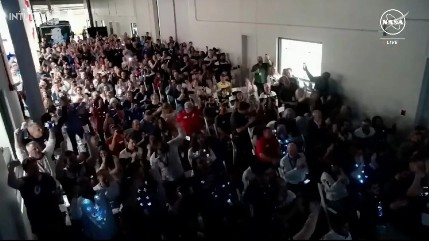 eine Menschenmenge in einem überfüllten Raum feiert, winkt mit den Armen und klatscht ab