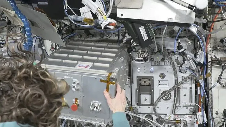 ein rack wird an der wand der internationalen raumstation installiert. man sieht den hinterkopf eines astronauten