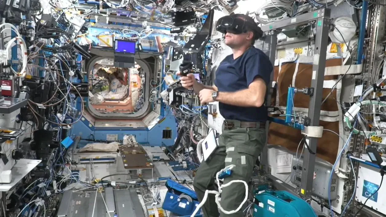 eine Person, die ein Headset in einem sehr überfüllten Modul der Internationalen Raumstation trägt, in dem alle Oberflächen mit Experimenten bedeckt sind