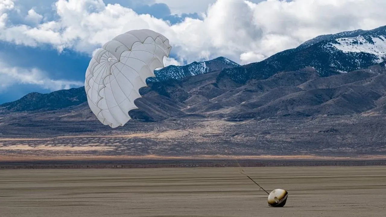 eine kegelförmige Kapsel liegt auf dem Wüstenboden, darüber weht ein Fallschirm im Wind