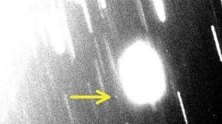 ein schwarz-weißes, unscharfes Bild mit vielen weißen Schlieren. In der rechten Mitte befindet sich ein weißer Fleck. Ganz links davon ist ein gelber Pfeil zu sehen.