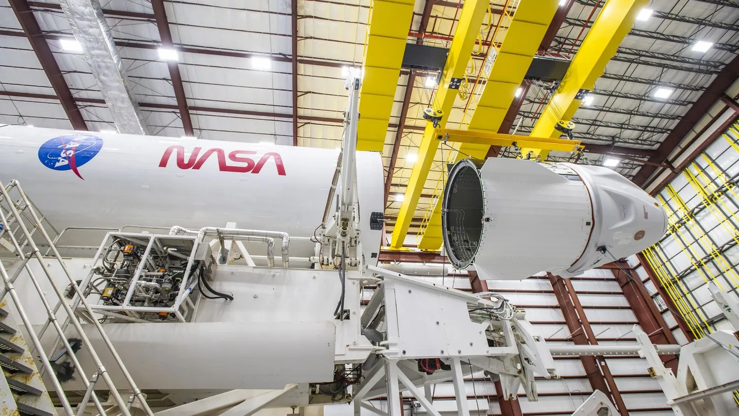 Eine weiße SpaceX-Endeavour-Dragon-Kapsel ist an ihre Falcon 9-Rakete gekoppelt, mit NASA-Logos auf weißem Hintergrund.