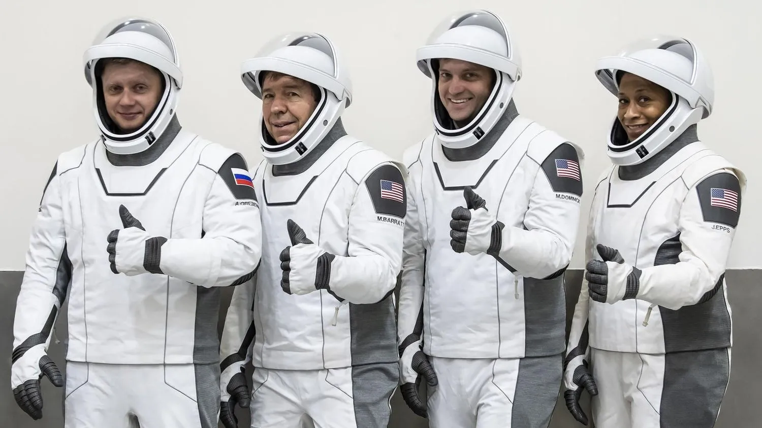 vier Astronauten mit weißen Raumanzügen und Helmen, die in einer Reihe stehend Daumen nach oben zeigen