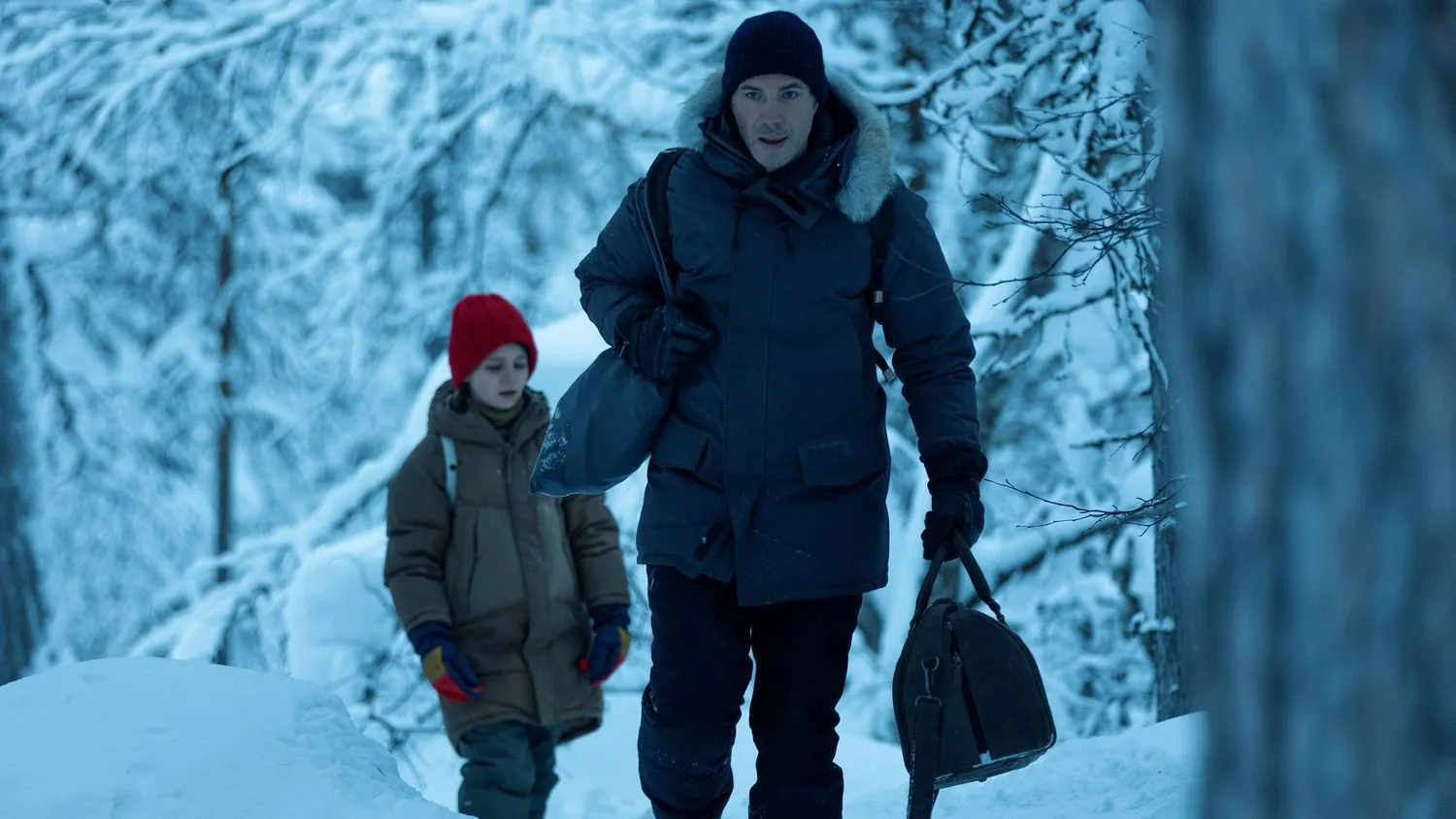 Ein junges Mädchen und ihr Vater tragen dicke Winterkleidung, als sie durch einen verschneiten Wald gehen.