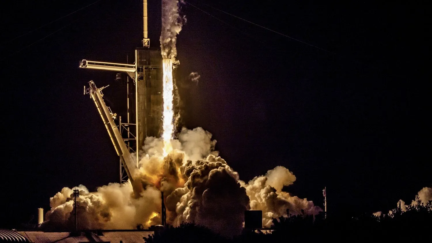 In der Dunkelheit der Nacht schießt eine Rakete aus ihren Triebwerken und schickt Rauchfahnen in die Luft, während sie den Startturm aus dem Bild klettert.