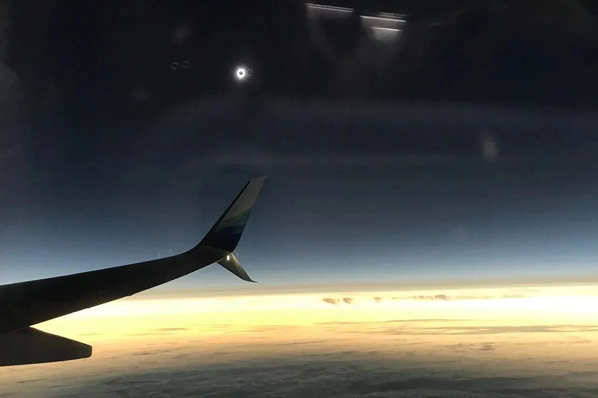 Blick auf eine Sonnenfinsternis in der Ferne über Wolken und einem Flugzeugflügel