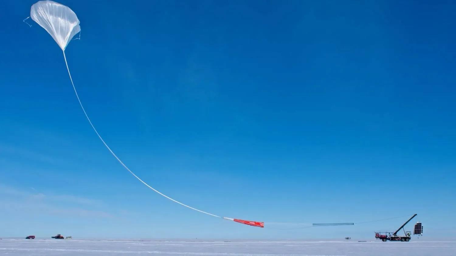 Ein großer weißer Wissenschaftsballon startet von einem flachen, schneebedeckten Fleck Erde in den blauen Himmel