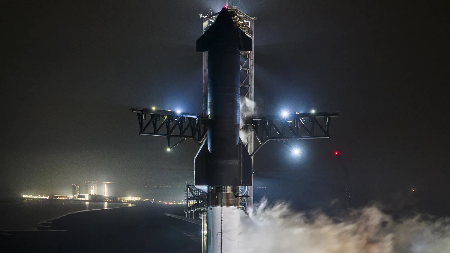 eine große schwarz-silberne Rakete stößt bei Nacht Dampf aus, während sie aufrecht auf einer Startrampe steht