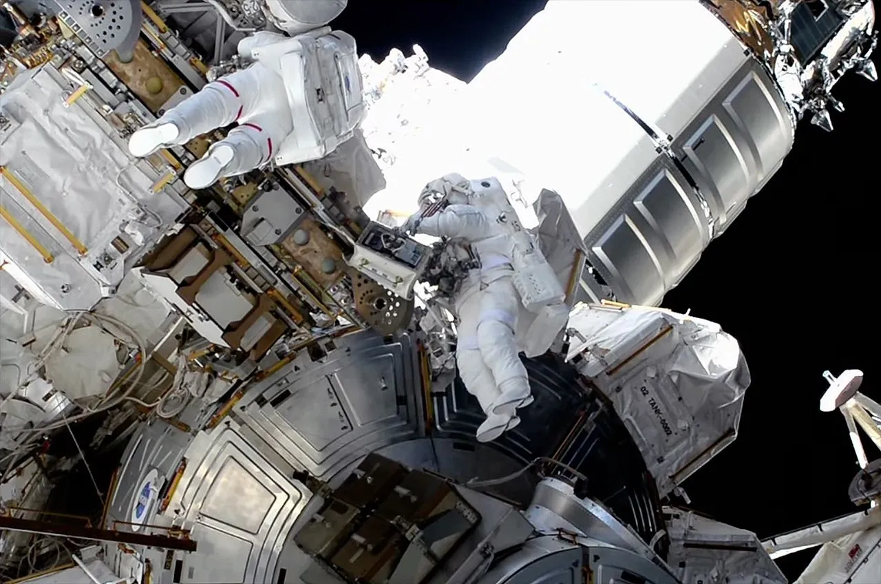 zwei Astronauten in Raumanzügen an der Außenseite einer Raumstation mit der Erde im Hintergrund