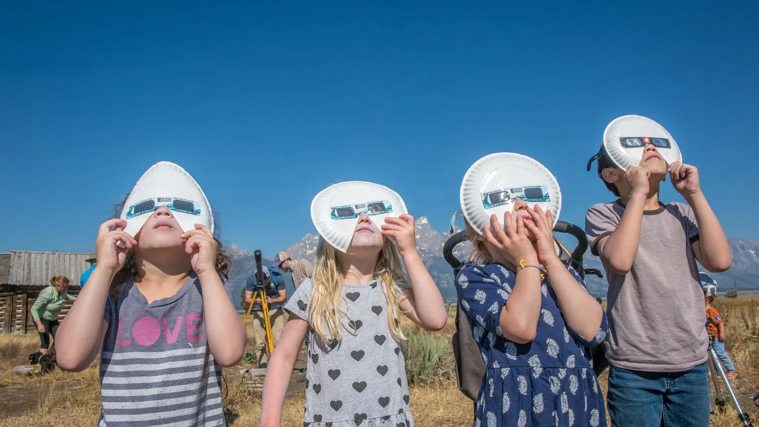 Gruppe von Kindern schaut mit Sonnenfinsternisbrillen nach oben, um die Sonnenfinsternis zu beobachten, Grand Tetons National Park, Teton County, Wyoming