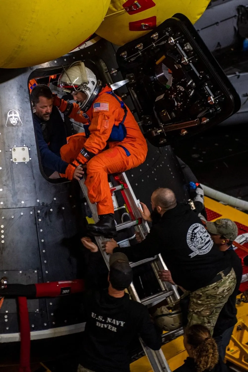ein Astronaut hockt vor einer offenen Raumschiffsluke in einem roten Fluganzug und Helm