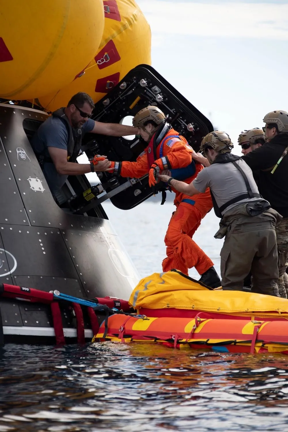 eine astronautin, die in ein raumschiff steigt, das auf einem floss im ozean schwimmt. die menschen um sie herum halten sie wegen des rauen wassers physisch aufrecht