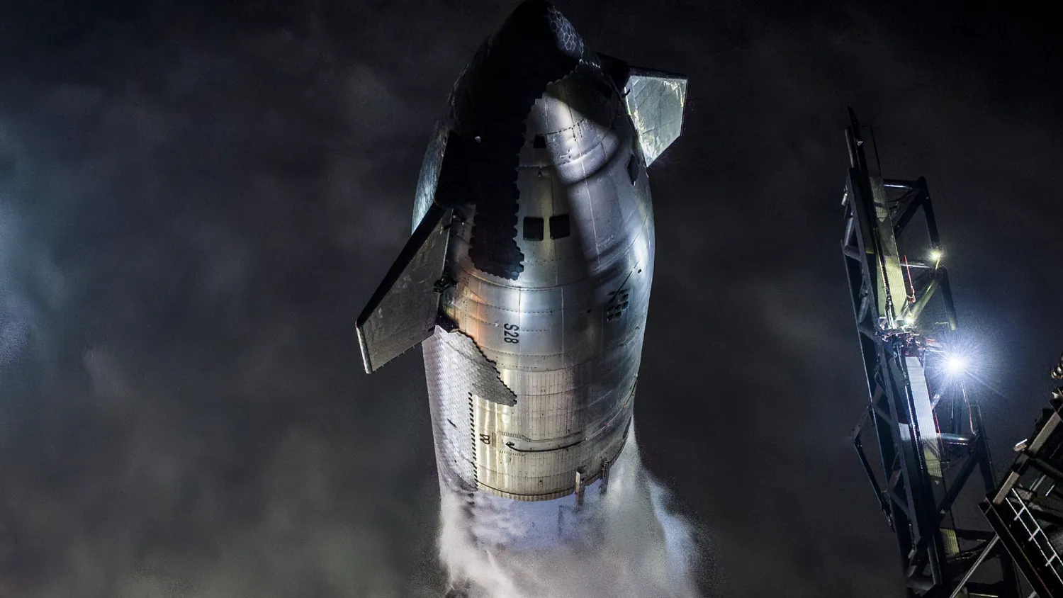 eine große schwarz-silberne Rakete stößt bei Nacht Dampf aus, während sie aufrecht auf einer Startrampe steht