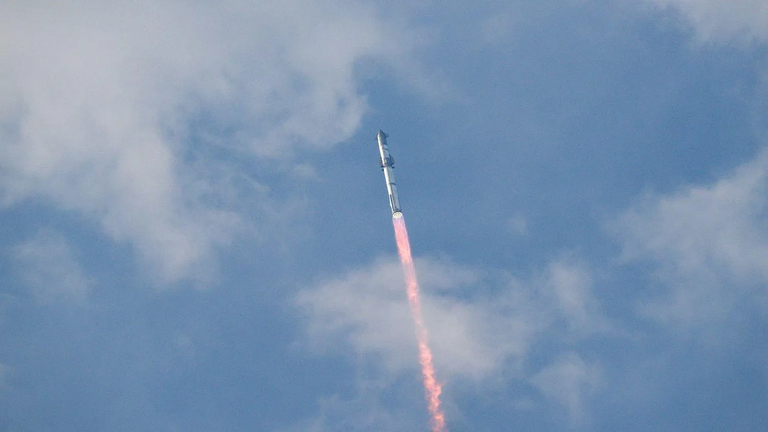 eine große silberne Rakete fliegt durch einen blauen Himmel über einer Flammensäule