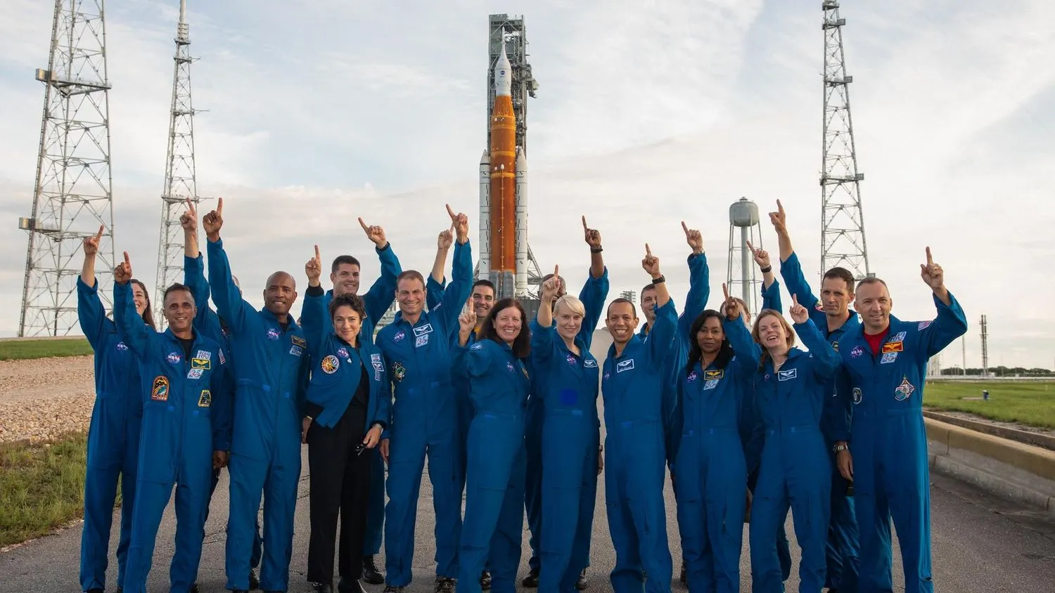 eine Gruppe von Astronauten in Fluganzügen, die vor einer riesigen Rakete stehen und in den Himmel zeigen