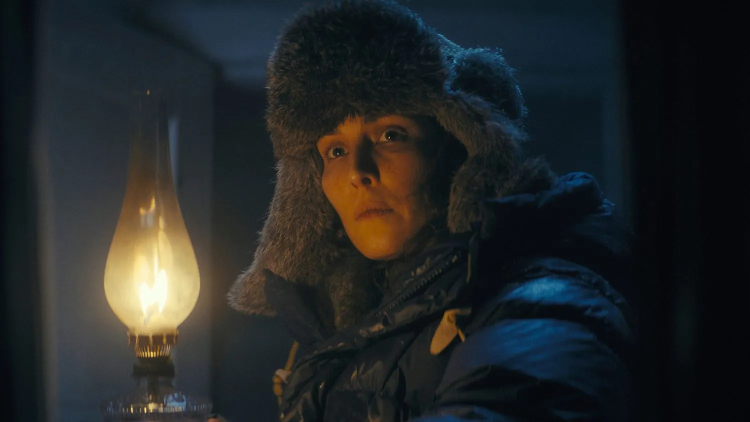 Frau hält eine brennende Lampe. Sie trägt eine dicke Wintermütze und eine Jacke