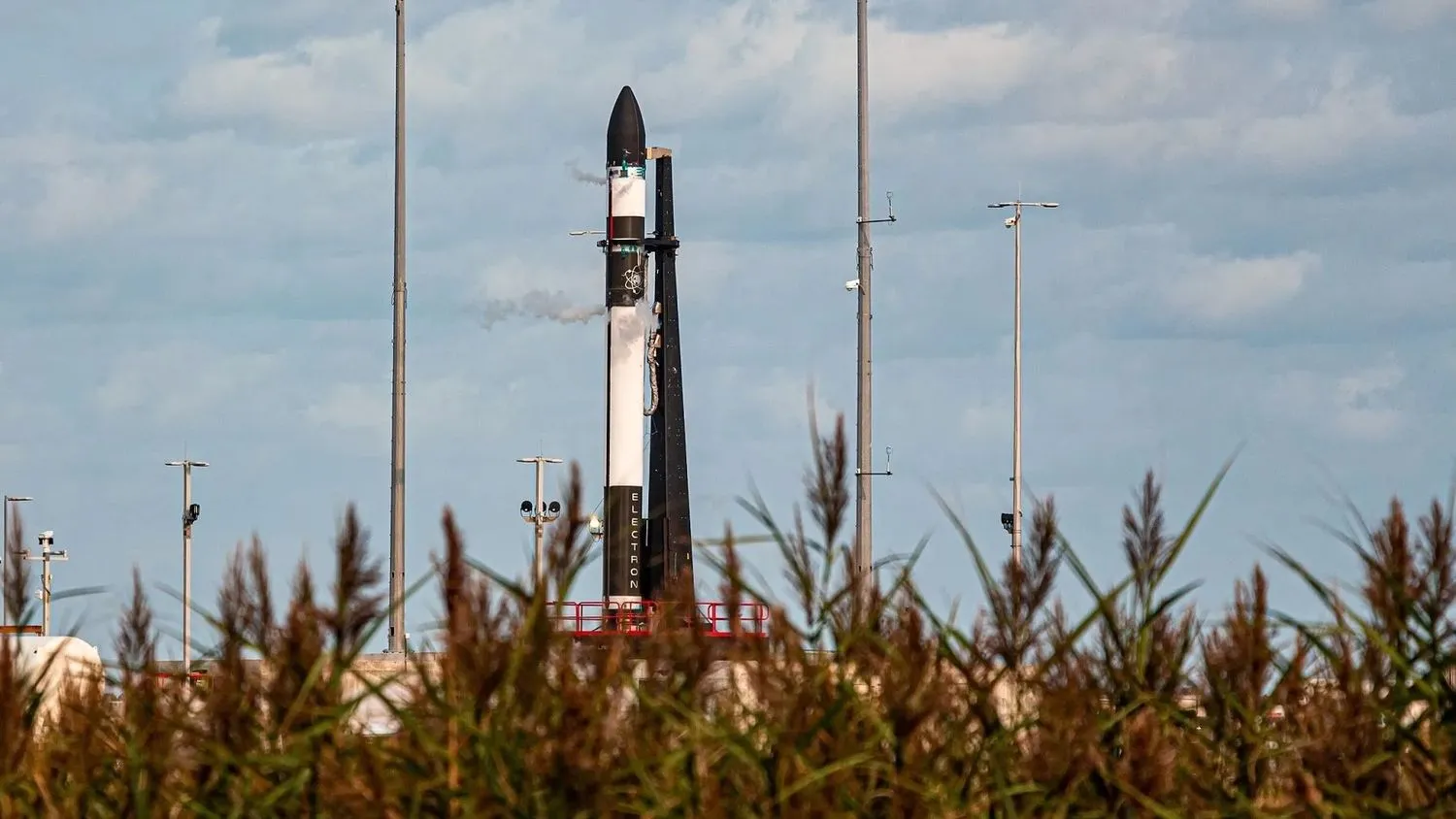 eine schwarz-weiße Rakete steht auf ihrer Startrampe, mit hohem Gras im Vordergrund