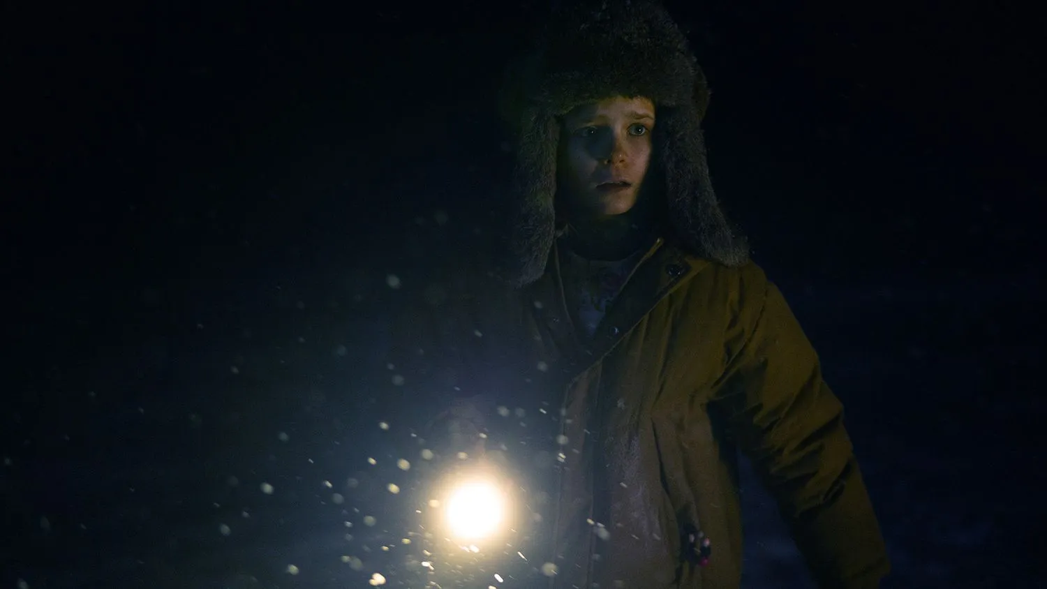 Ein junges Mädchen hält eine Taschenlampe in der Hand und sucht im Dunkeln. Sie trägt eine dicke Wintermütze und eine Jacke.