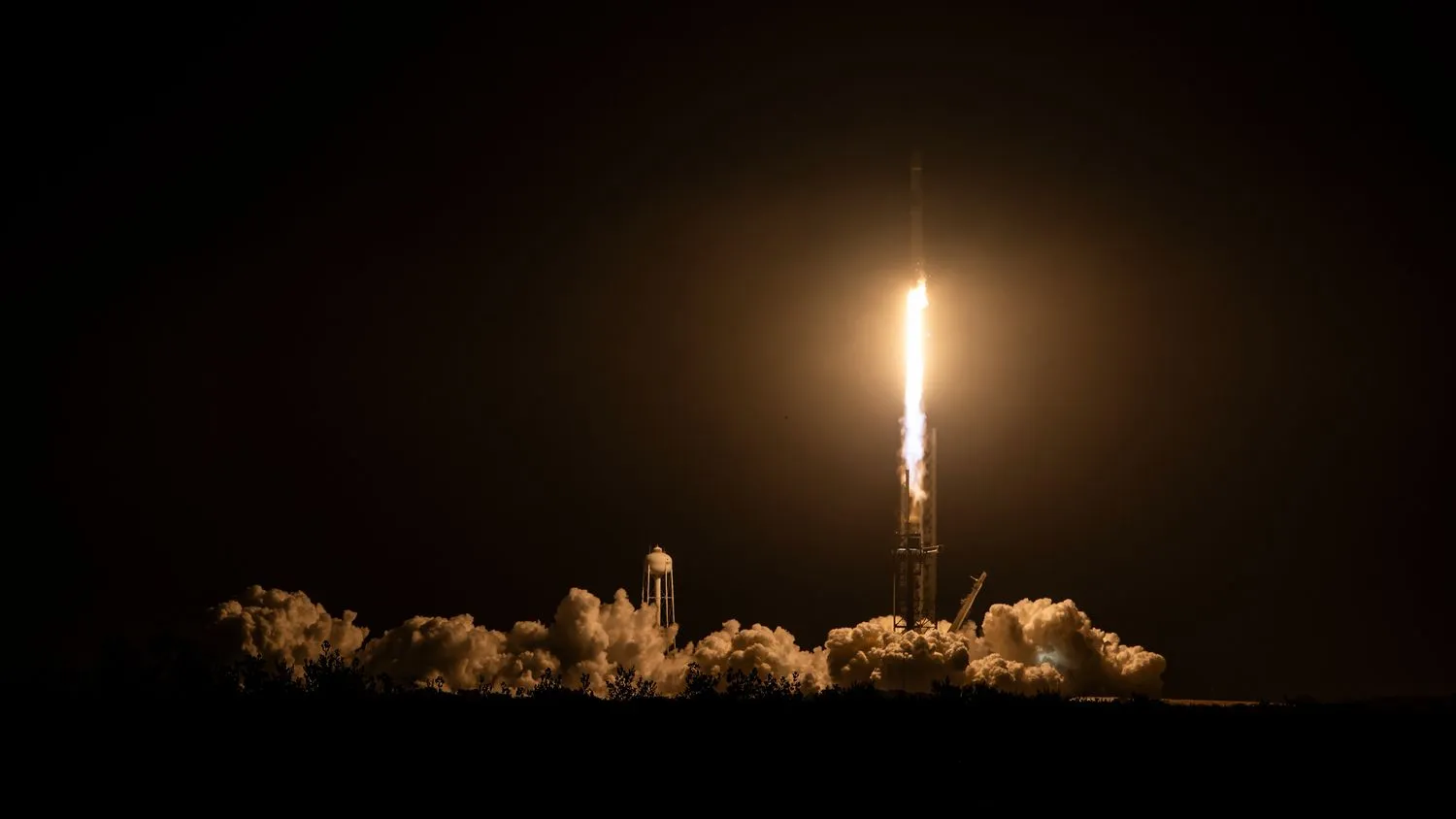 eine schwarz-weiße SpaceX Falcon 9 Rakete startet in den Nachthimmel.