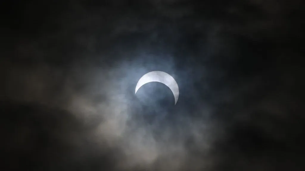 Partielle Sonnenfinsternis durch Wolken. Die Sonne scheint die Form einer Sichel anzunehmen, während der Mond einen Bissen aus der Sonne zu nehmen scheint.