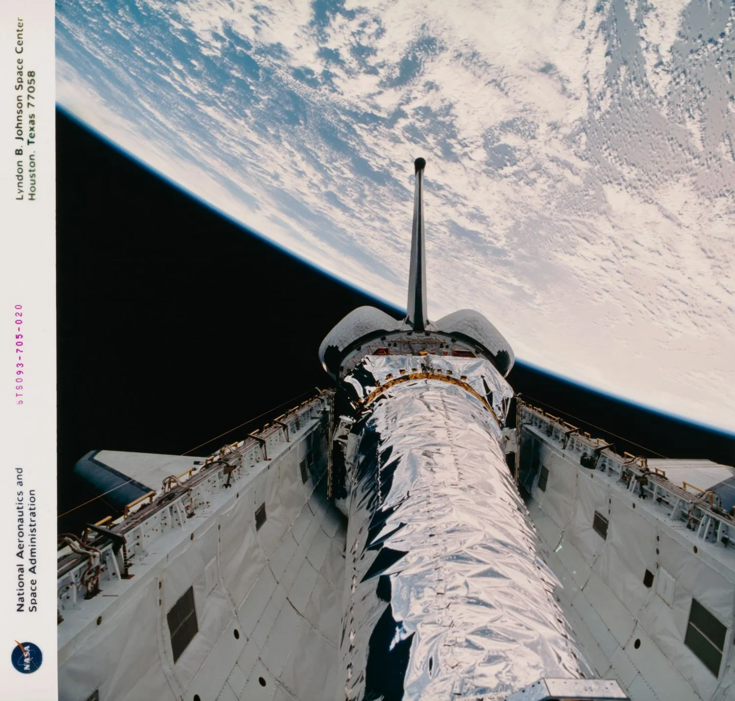 ein glänzendes Raumschiff ruht im weißen Frachtraum eines Space Shuttles mit einer großen Fläche der Erde im Hintergrund.